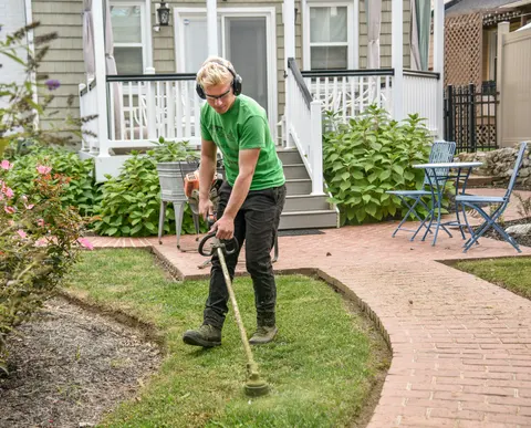 A landscaper edging a lawn along a brick path in front of a porch